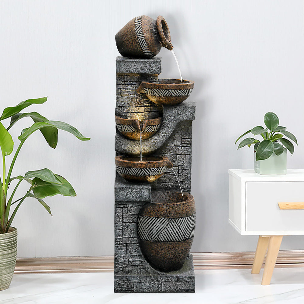 Resin Carved Clay Urn Outdoor Water Fountain 42 Inch displayed indoors between leafy plants and a white side table.