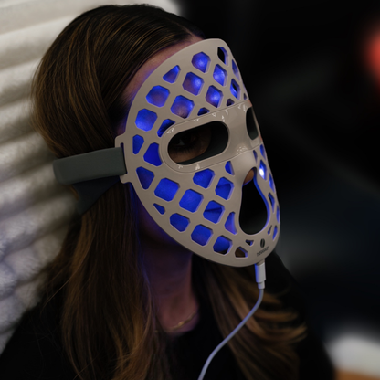 A woman reclines wearing the blue-lit TheraGlow Mask2Go+™ LED Light Therapy Face Mask, viewed from the side.