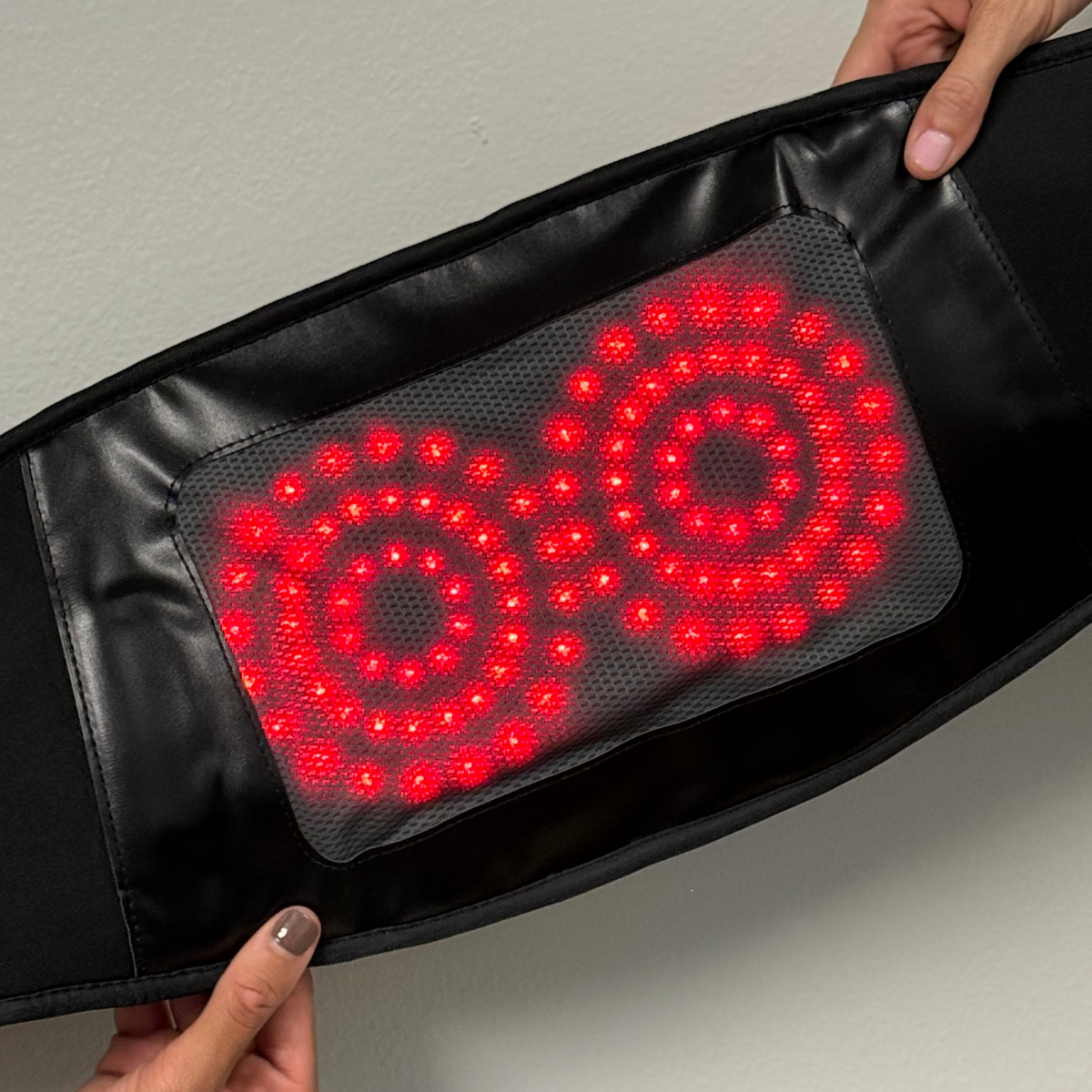 Close-up of the glowing red light panel inside the TheraBelt Red Light Therapy Recovery Belt, held open by hands.
