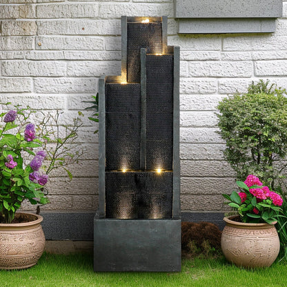 Resin Ribbed Slate Outdoor Water Fountain Quiet 50 in is centered between flowering pots against a light brick wall.
