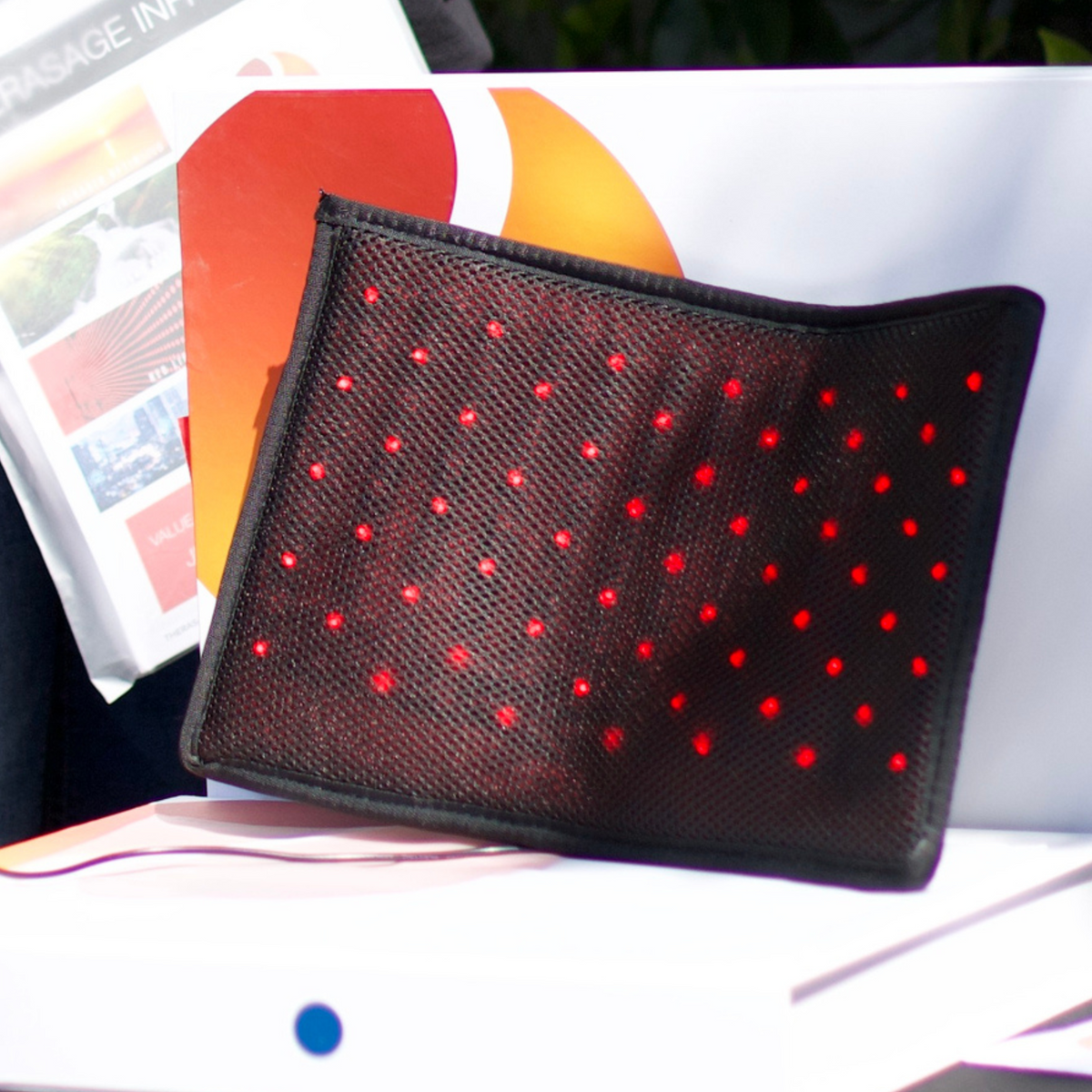 Therasage Tri-Lite™ Red Light Therapy Panel leans on a white display surface with red lights glowing beside brochures.