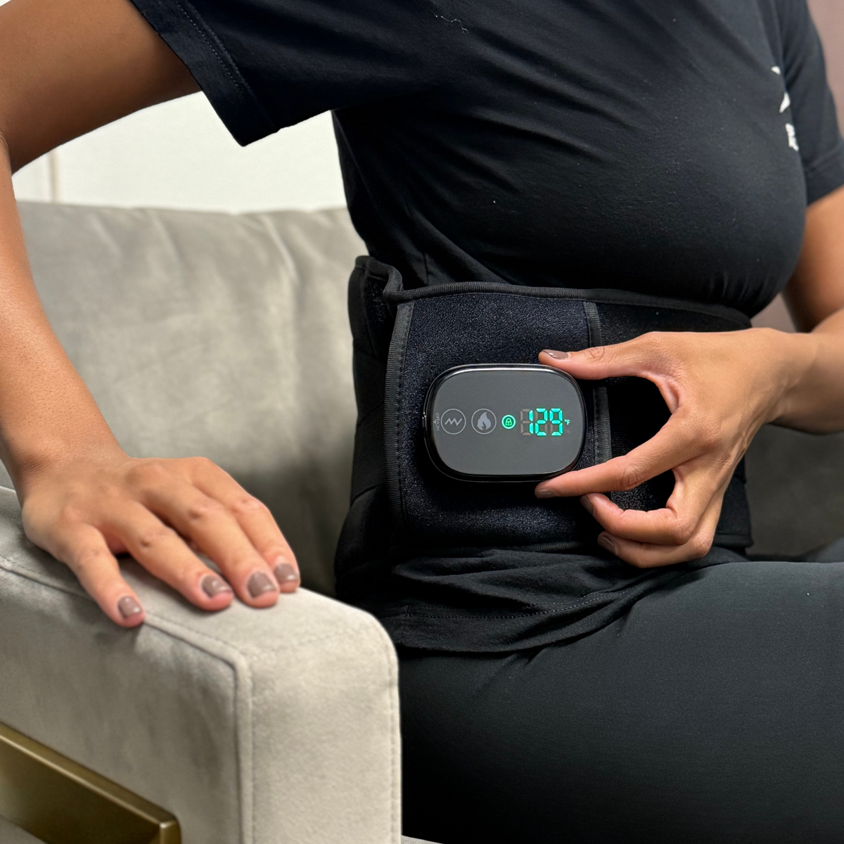 A seated person adjusts the digital display on the TheraBelt Red Light Therapy Recovery Belt worn around the waist.