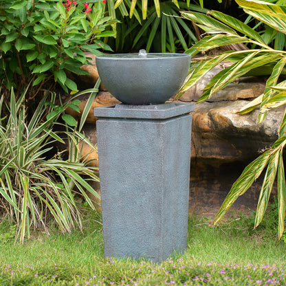 Resin Zen Bowl Pedestal Outdoor Fountain 35 Inch bubbling in a lush garden among rocks and leafy plants.