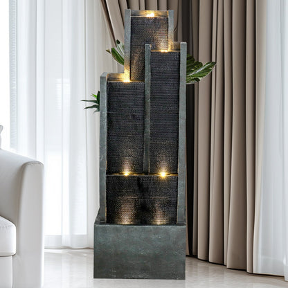 Resin Ribbed Slate Outdoor Water Fountain Quiet 50 in stands indoors beside a white chair, curtains, and a leafy plant.