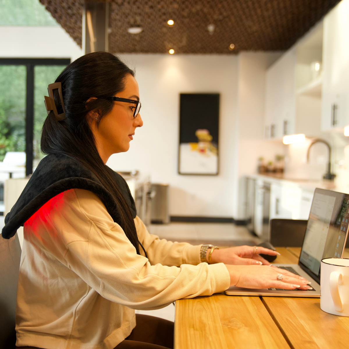 A woman works at a laptop with the TheraPerfect Pad™ across her shoulders in a home office.