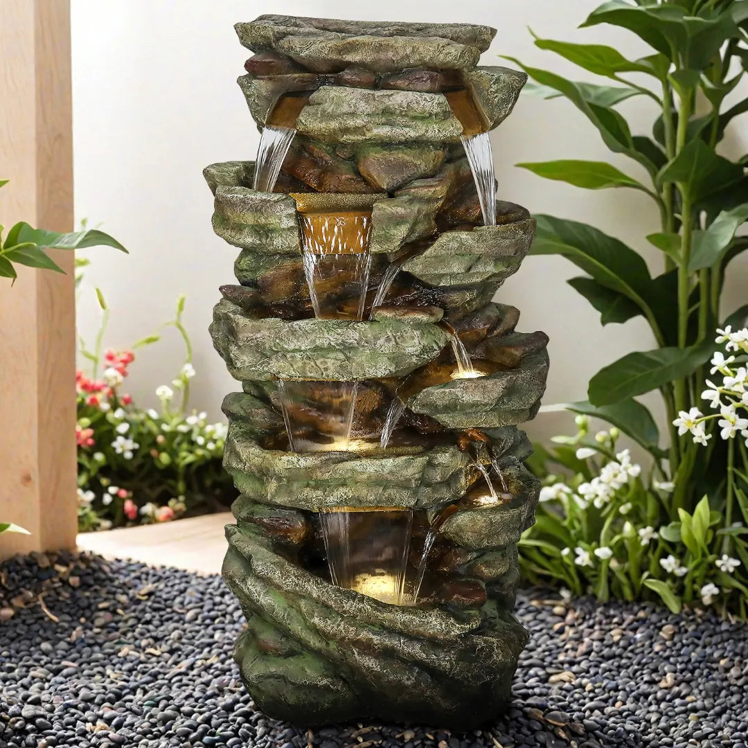 Resin Stacked Stone Rock Waterfall Outdoor Fountain pours into tiered basins among garden plants and gravel.
