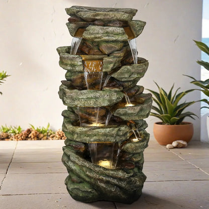 Resin Stacked Stone Rock Waterfall Outdoor Fountain shown on a paved patio beside a potted plant.