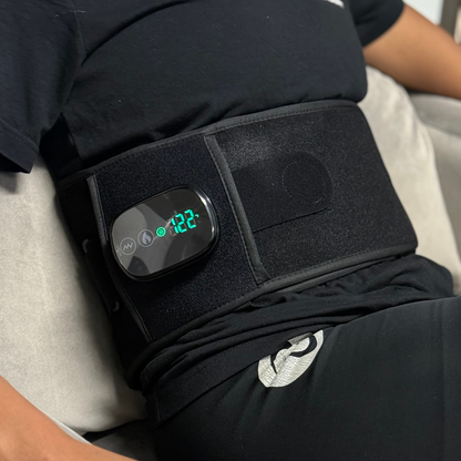 Close-up of the TheraBelt Red Light Therapy Recovery Belt wrapped around a seated person's waist, showing its lit display.