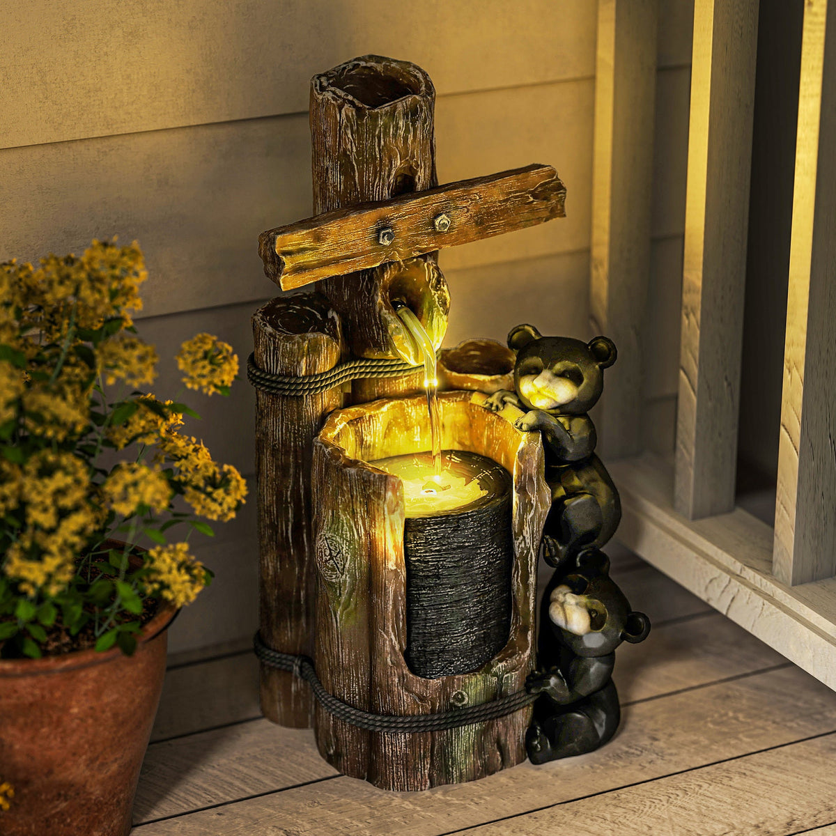 Resin Bear Fountain Two Cubs on Timber Post with water flowing into a glowing basin beside a potted plant.