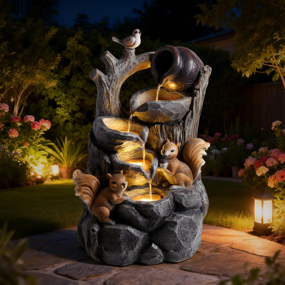 Resin Squirrel Tree Stump Outdoor Fountain 30 Inch LED glows at night on a garden patio surrounded by plants.