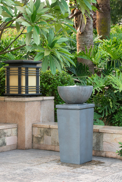 Resin Zen Bowl Pedestal Outdoor Fountain 35 Inch on a paved patio beside a garden lantern and greenery.