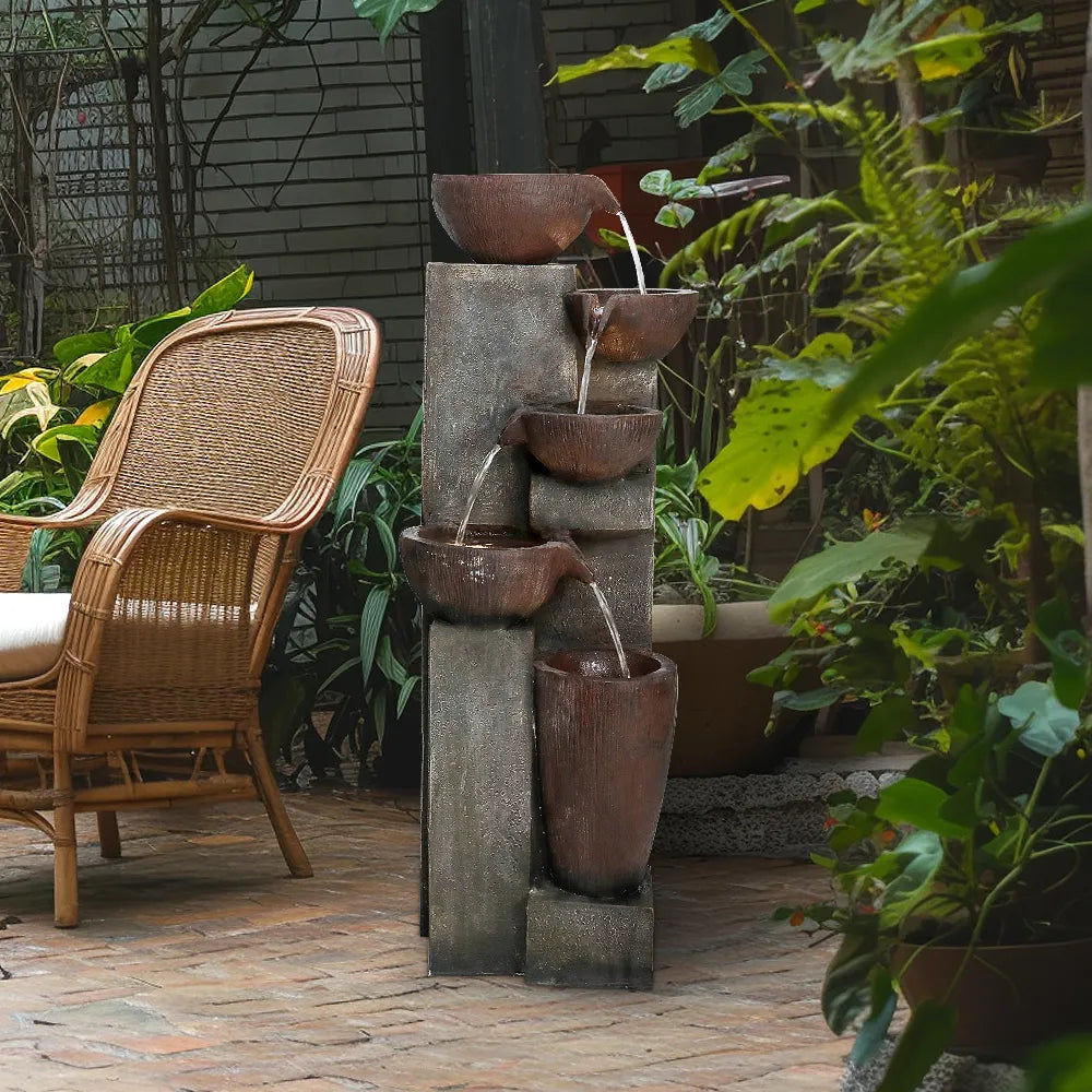 Resin Diagonal Cascading Floor Fountain Outdoor 40 in on a brick patio beside a wicker chair and leafy plants.