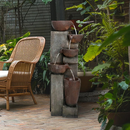 Resin Diagonal Cascading Floor Fountain Outdoor 40 in on a brick patio beside a wicker chair and leafy plants.