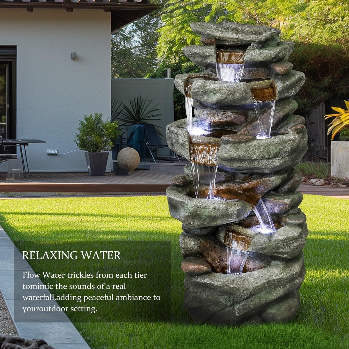 Resin Overhanging Ledge Rock Waterfall Fountain Outdoor stands on a lawn beside a modern home's patio.