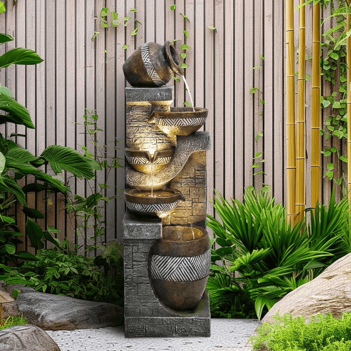 Resin Carved Clay Urn Outdoor Water Fountain 42 Inch flows among tropical plants beside a slatted garden screen.