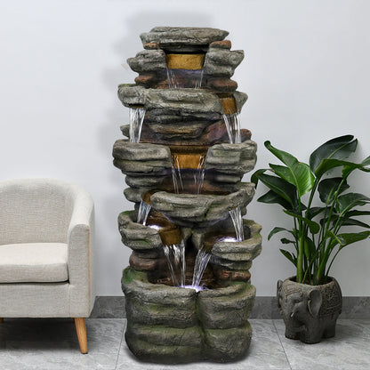 Resin Stepped Shale Outdoor Rock Fountain with cascading water indoors, beside a white chair and leafy plant.