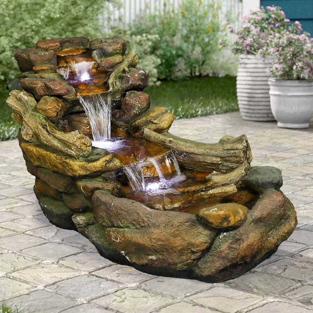 Resin Driftwood Creek Horizontal Outdoor Fountain 39 in on a stone patio near flowering planters.