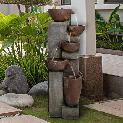 Resin Diagonal Cascading Floor Fountain Outdoor 40 in among tropical leaves and smooth garden stones.