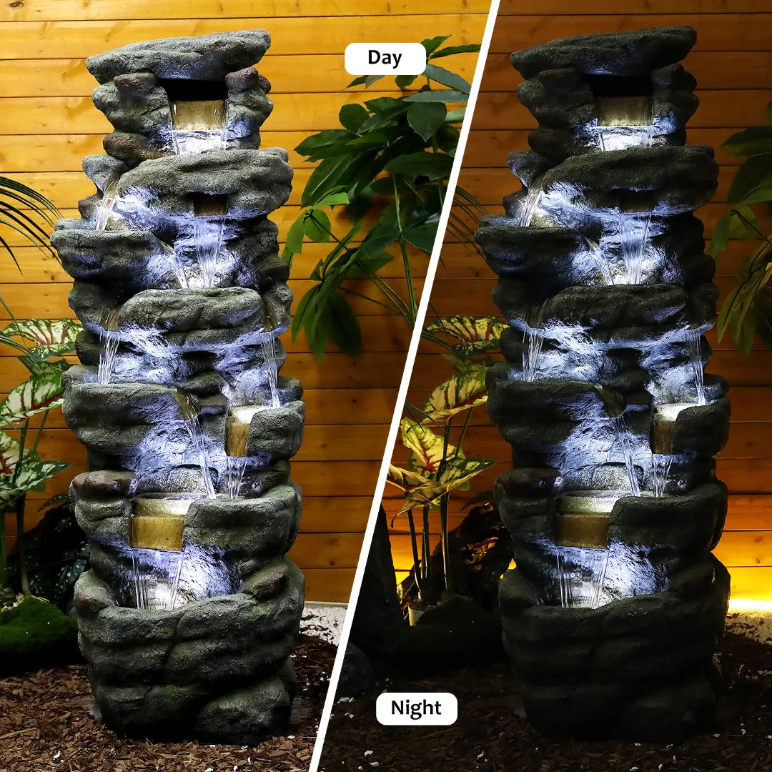 Resin River Rock Outdoor Fountain Pillar 51 Inch 52 lb shown flowing by day and illuminated at night against a wood wall.