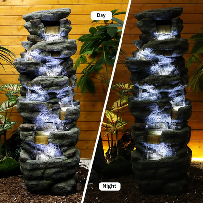 Resin River Rock Outdoor Fountain Pillar 51 Inch 52 lb shown flowing by day and illuminated at night against a wood wall.