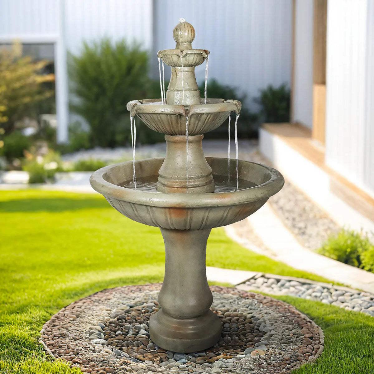 Concrete Fluted 3 Tier Outdoor Water Fountain 51 Inch shown full view in a garden with lawn and shrubs.