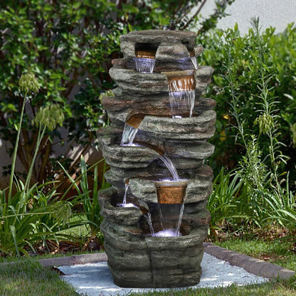 Resin Serpentine Slate Column Cascading Outdoor Fountain centered among dense green garden plants.