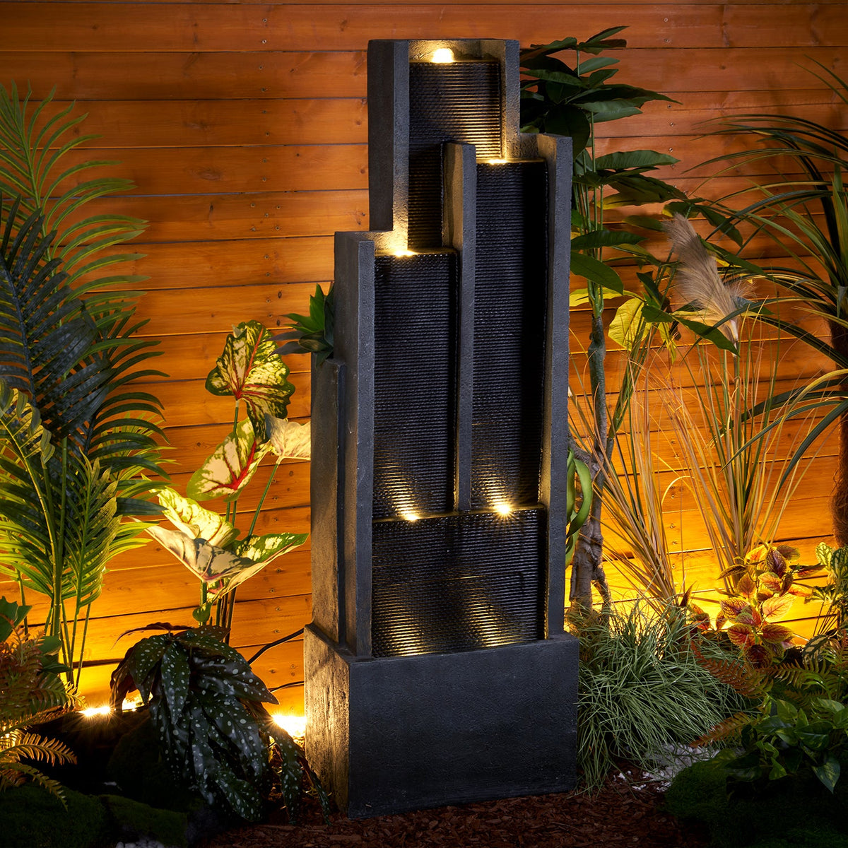 Resin Ribbed Slate Outdoor Water Fountain Quiet 50 in shown from an angled view among garden plants and warm lights.