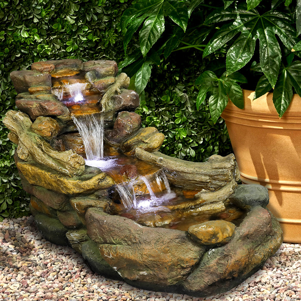 Resin Driftwood Creek Horizontal Outdoor Fountain 39 in beside a leafy potted plant and gravel.