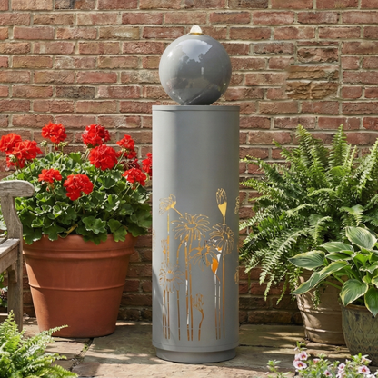 Metal Sphere Water Fountain Outdoor shown full-length between potted red flowers and ferns against a brick wall.