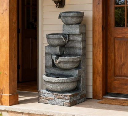 Resin Offset Bowl Cascading Outdoor Water Fountain stands beside a wooden front door and light-colored siding.