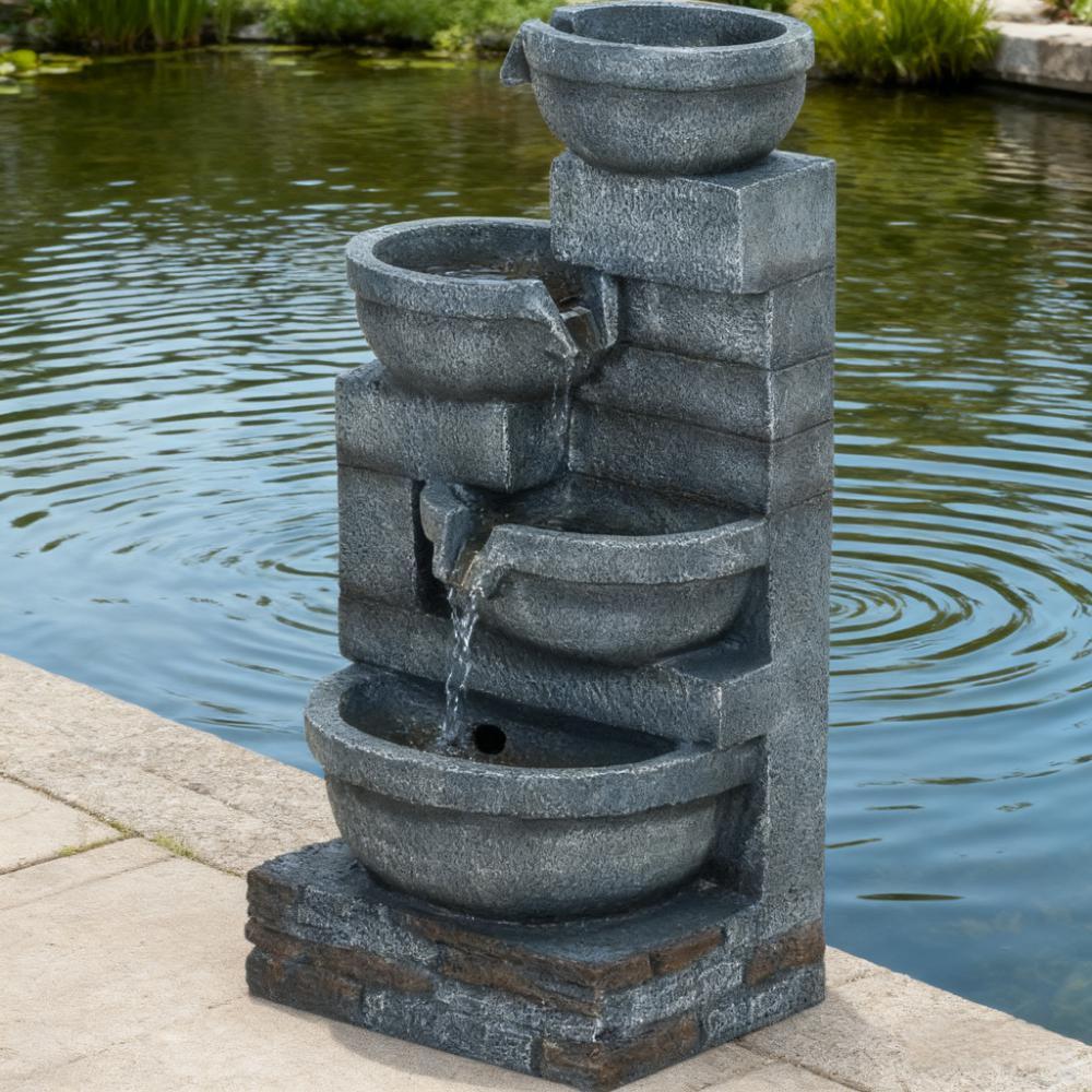 Resin Offset Bowl Cascading Outdoor Water Fountain pours into tiered basins beside a pond and stone patio.