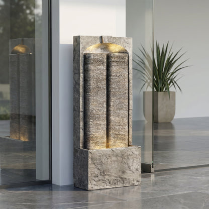 Resin Slate Outdoor Water Wall Fountain stands beside glass doors with a potted plant nearby.
