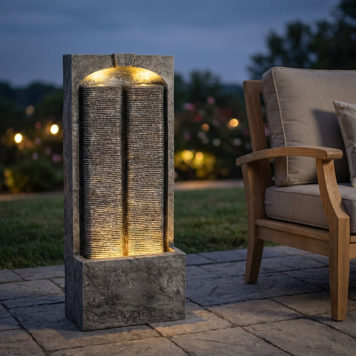 Resin Slate Outdoor Water Wall Fountain glows beside a cushioned patio chair at dusk.