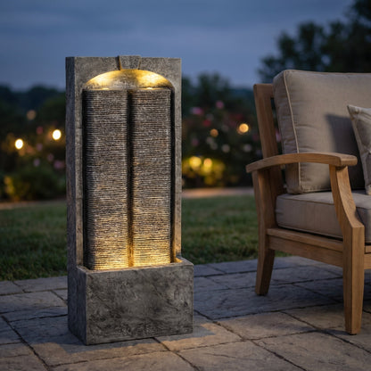 Resin Slate Outdoor Water Wall Fountain glows beside a cushioned patio chair at dusk.