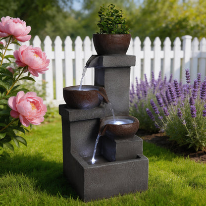 Resin Outdoor Fountain and Planter Stacked Stone stands by a white picket fence among peonies and lavender.