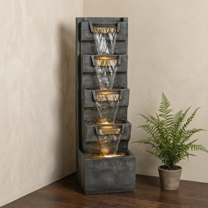 Resin Modern Outdoor Fountain 39 Inch Tilted Chutes stands beside a potted fern against a light wall.