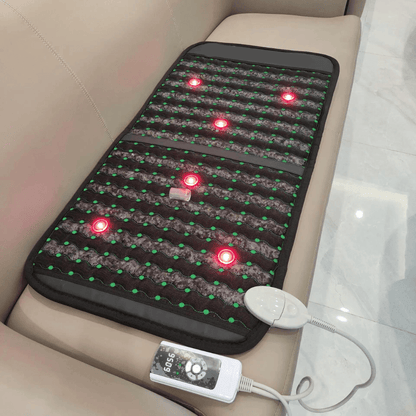 Infrared PEMF Travel Mat spread across a beige sofa, with glowing red points and a wired controller beside it.